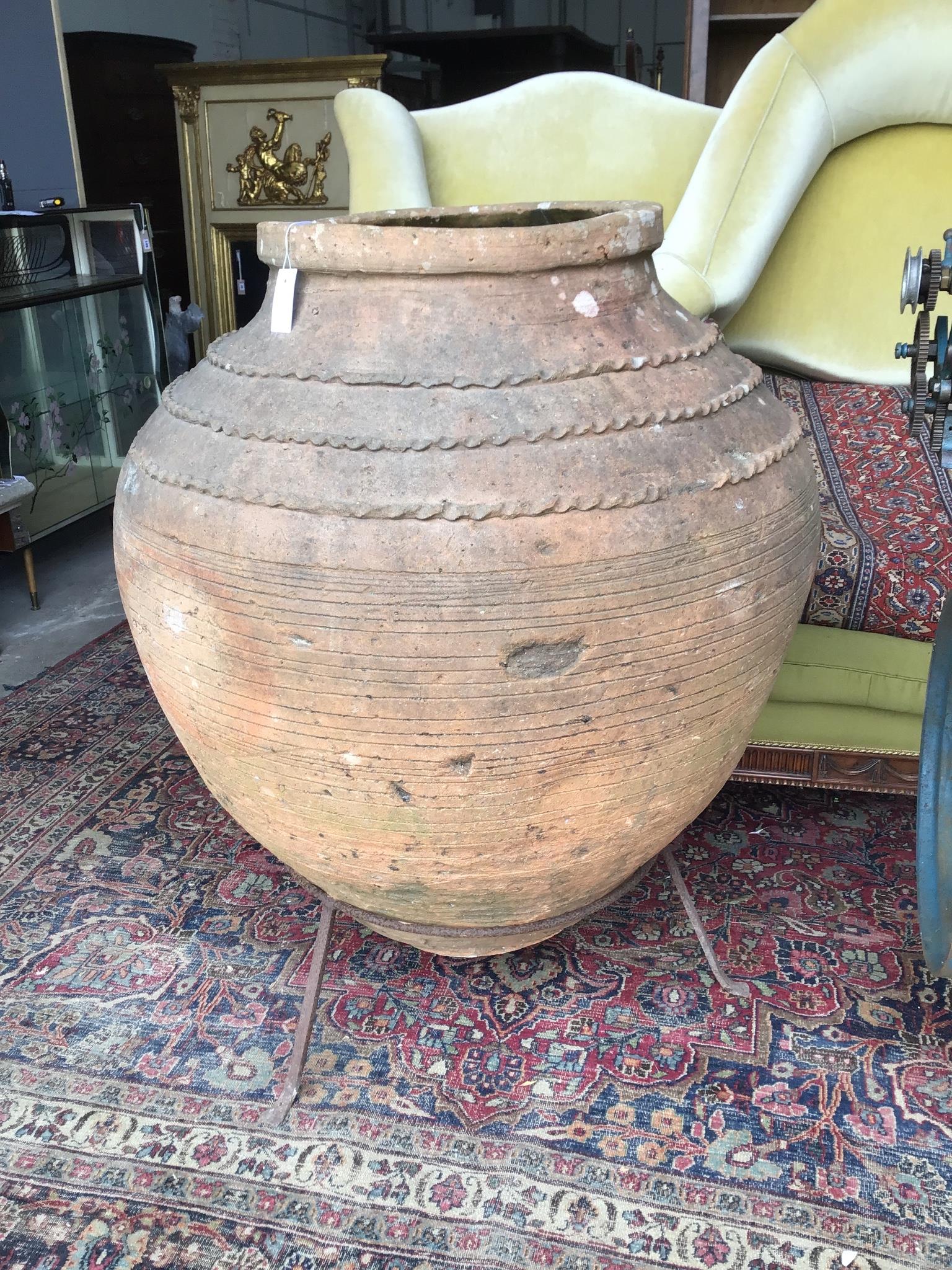 A large antique Greek style earthenware olive jar on wrought iron stand, height 116cm